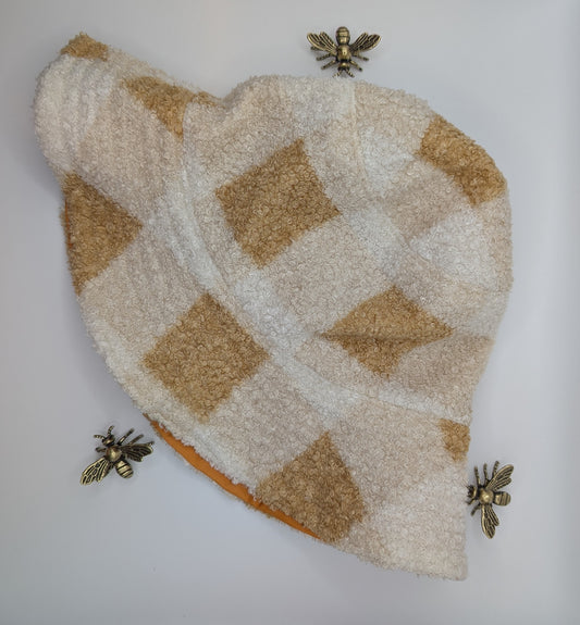 A beige and white checkered bucket hat with a fleece texture, displayed with bees around it.